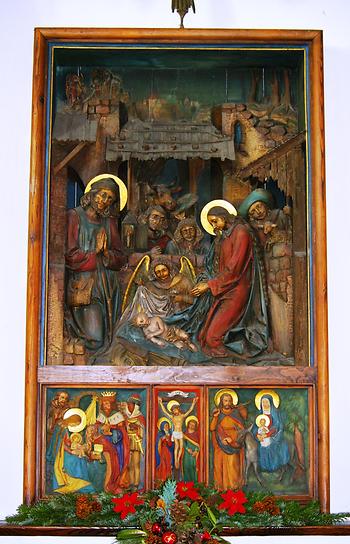 Altar in der Stille-Nacht-Kapelle. Oben 'Geburt Christi' (Weihnachtskrippe), Hermann Hutter (1915) - Unten 'Anbetung der Könige', 'Kreuzigung', 'Flucht nach Ägypten', Max Domenig, in Hallein 1936 geschnitzt - Foto: Werner100359, Wikimedia Commons - Gemeinfrei