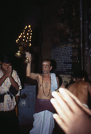 A temple servant blesses the pilgrims with a large chandelier A temple servant blesses the pilgrims with a large chandelier